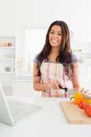 Attractive woman relaxing with her laptop while cooking vegetabl