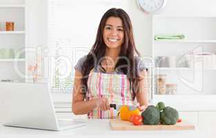 Beautiful woman relaxing with her laptop while cooking vegetable
