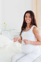 Pretty pregnant woman holding a glass of water and pills while s
