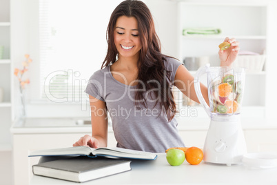 Charming woman consulting a notebook while filling a blender wit