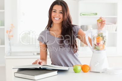 Beautiful woman consulting a notebook while filling a blender wi