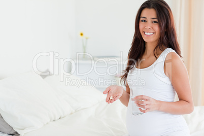 Beautiful pregnant woman holding a glass of water and pills whil