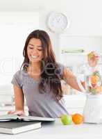 Attractive woman consulting a notebook while filling a blender w