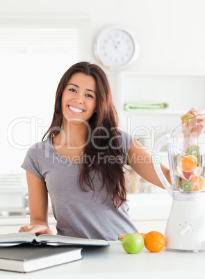 Good looking woman consulting a notebook while filling a blender