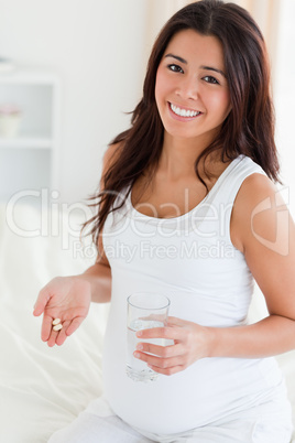 Attractive pregnant woman holding a glass of water and pills whi