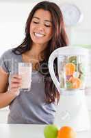 Good looking woman using a blender while holding a drink
