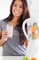 Charming woman using a blender while holding a drink