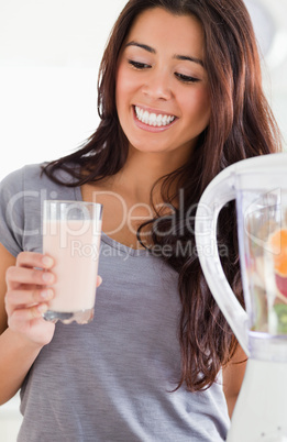 Pretty woman using a blender while holding a drink