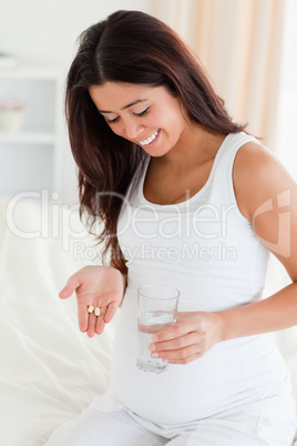 Good looking pregnant woman holding a glass of water and pills w