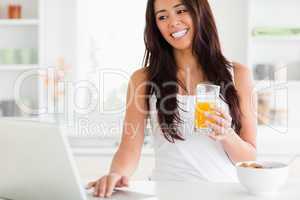 Charming woman relaxing with her laptop while holding a glass of