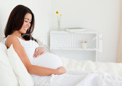 Beautiful pregnant woman touching her belly while lying on a bed