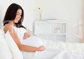 Beautiful pregnant woman touching her belly while lying on a bed