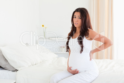 Attractive pregnant woman holding her back while sitting on a be