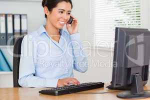 Attractive woman using her mobile phone while typing on a keyboa