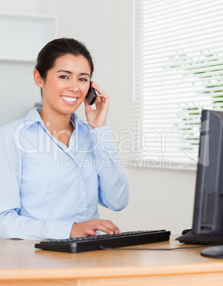 Good looking woman using her mobile phone while typing on a keyb