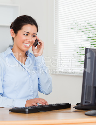 Charming woman using her mobile phone while typing on a keyboard