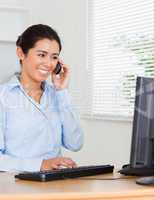 Charming woman using her mobile phone while typing on a keyboard