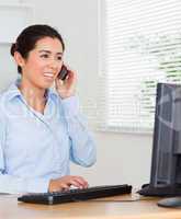 Lovely woman using her mobile phone while typing on a keyboard