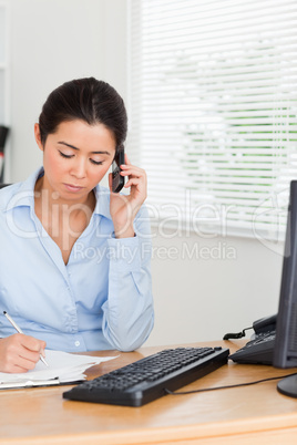 Lovely woman using her mobile phone while writing on a sheet of