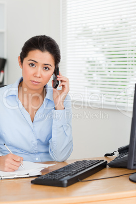 Beautiful woman using her mobile phone while writing on a sheet