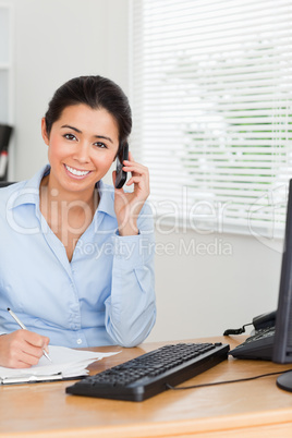Attractive woman using her mobile phone while writing on a sheet
