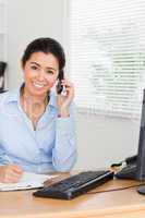 Attractive woman using her mobile phone while writing on a sheet