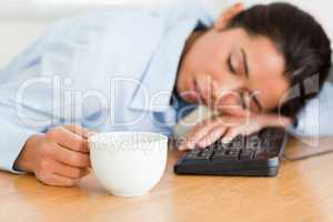 Beautiful woman sleeping on a keyboard while holding a cup of co