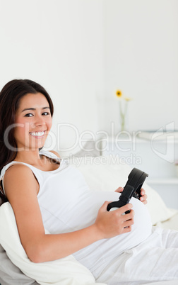 Attractive pregnant woman putting headphones on her belly while