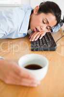 Gorgeous woman sleeping on a keyboard while holding a cup of cof