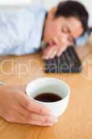 Cute woman sleeping on a keyboard while holding a cup of coffee