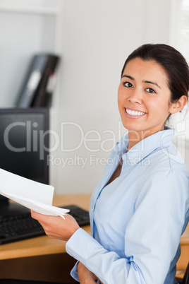 Beautiful woman holding a sheet of paper and posing while sittin