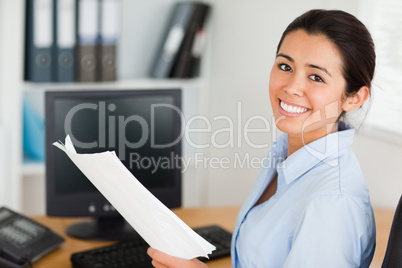 Attractive woman holding a sheet of paper and posing while sitti
