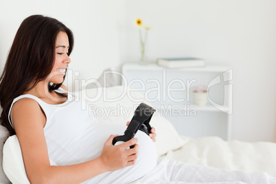 Good looking pregnant woman putting headphones on her belly whil