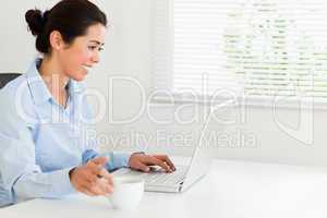 Charming woman relaxing with her laptop while enjoying a cup of