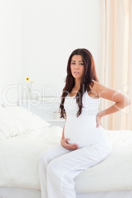 Good looking pregnant woman holding her back while sitting on a