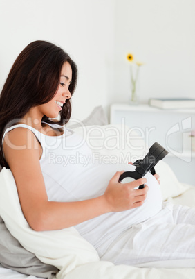 Charming pregnant woman putting headphones on her belly while ly
