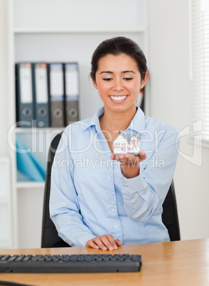 Attractive woman holding a miniature house while looking at the