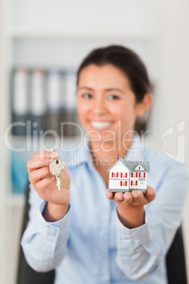 Beautiful woman holding keys and a miniature house while looking