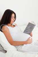 Charming pregnant woman reading a book while lying on a bed