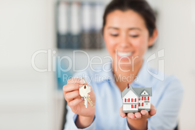 Charming woman holding keys and a miniature house while looking