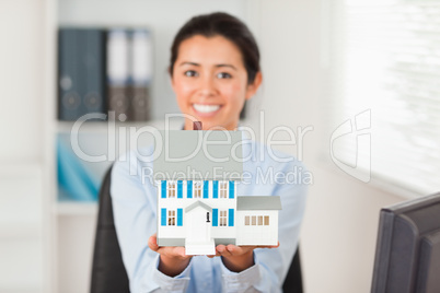 Lovely woman holding a miniature house while looking at the came