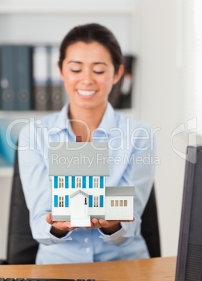 Pretty woman holding a miniature house while looking at the came