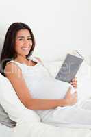 Attractive pregnant woman reading a book while lying on a bed