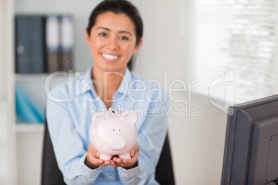 Attractive woman holding a piggy bank while looking at the camer