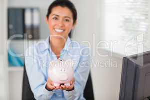 Attractive woman holding a piggy bank while looking at the camer