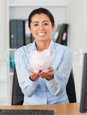 Good looking woman holding a piggy bank while looking at the cam