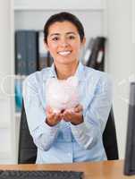 Good looking woman holding a piggy bank while looking at the cam