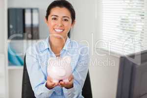 Beautiful woman holding a piggy bank while looking at the camera