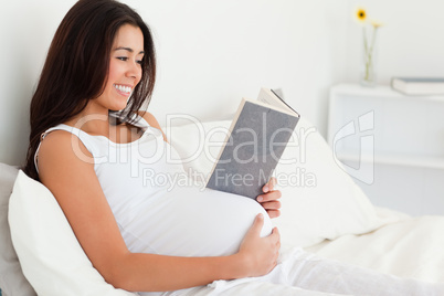 Good looking pregnant woman reading a book while lying on a bed