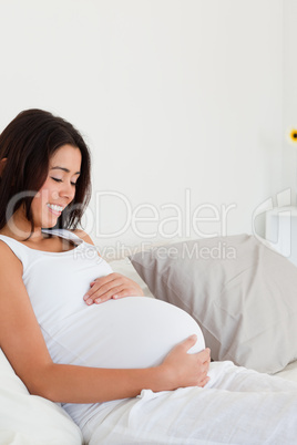 Gorgeous pregnant woman touching her belly while lying on a bed